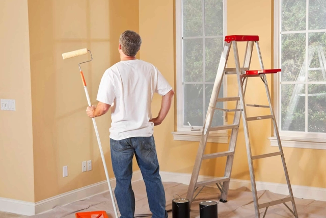 Painter in a Room with Paint Roller and Ladder, Preparing to Refinish Walls
