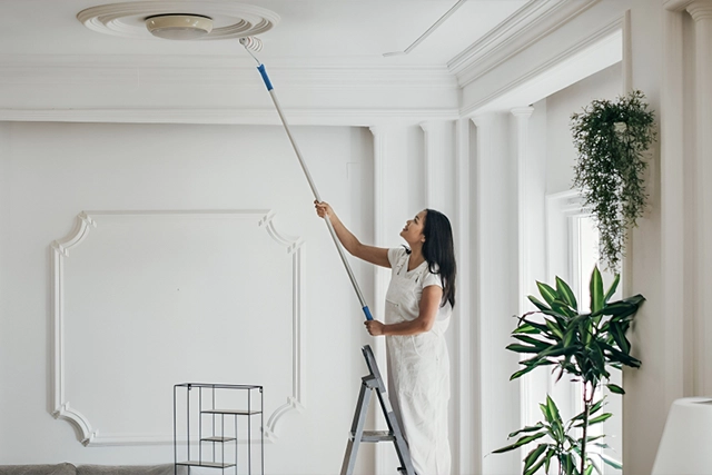 Woman Painting Ceiling with Long Roller in Bright Room