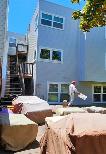 Painter Working on Exterior of Modern House with Covered Furniture
