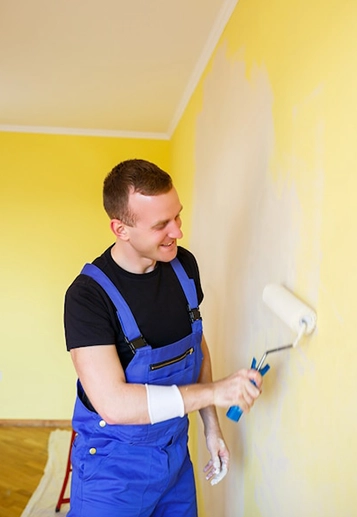 Man in Blue Overalls Painting Yellow Wall with Roller Brush